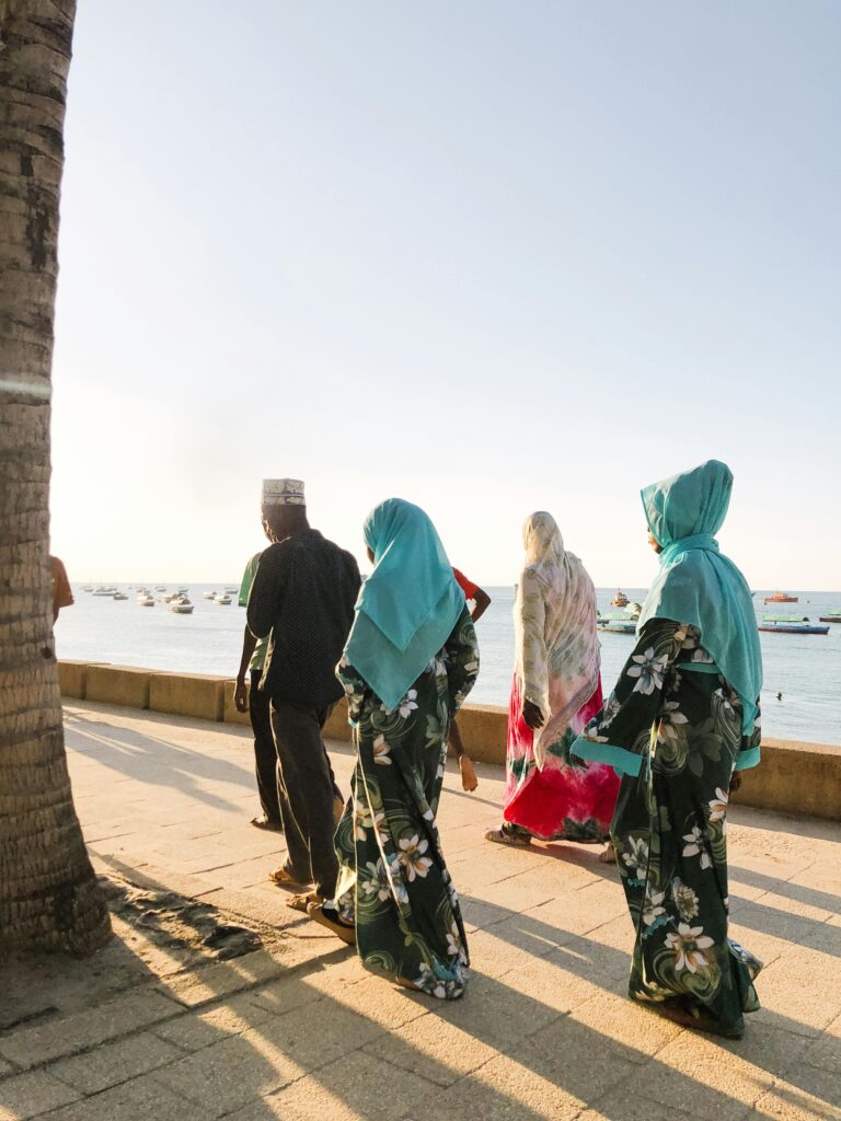 People in traditional attire walking by the ocean in Zanzibar, Tanzania, at golden hour.